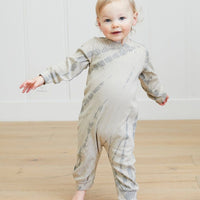 Child wearing a gray and white striped onesie standing on a wooden floor.