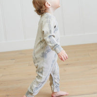 Child wearing a tie-dye onesie standing on a wooden floor.