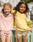 Three young girls standing together outdoors, wearing colorful outfits.