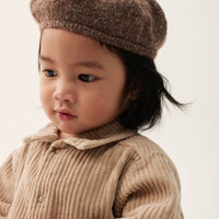 Child wearing a brown knit hat and matching outfit against a plain background
