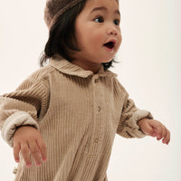 Child wearing a beige ribbed outfit and hat on a white background