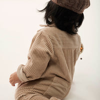 Person wearing a beige knitted outfit and brown beret on a white background
