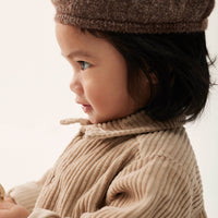 Child wearing a brown knitted hat and beige sweater against a neutral background