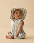 Baby wearing a striped romper and hat on a beige background