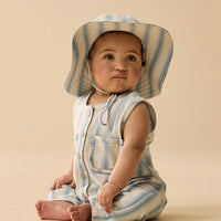 Baby wearing a striped romper and hat on a beige background