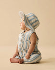 Baby wearing a striped romper and bonnet on a beige background