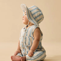 Baby wearing a striped romper and bonnet on a beige background
