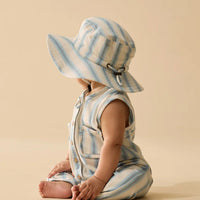 Baby in a striped romper and sun hat sitting on a beige background
