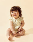 Baby sitting on a beige surface wearing a lace romper.