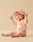 Baby in pink outfit and hat sitting on a beige background