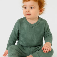 Baby wearing a green outfit sitting on a white background