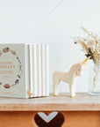 Book titled 'Our Little Library' on a wooden shelf with a unicorn figurine and vase of dried flowers.