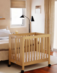 Wooden crib in a bedroom with a bed and window in the background