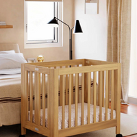 Wooden crib in a bedroom with a bed and window in the background
