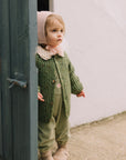 Child wearing a green knitted outfit peeking out from behind a door.