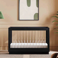 Modern black crib in a stylish room with abstract art, lamp, and plant.