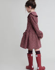 Child wearing a patterned coat and red rain boots on a plain background