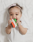 Baby lying on a white blanket with a colorful teething toy.