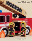 Toy fire truck with wooden ladder and firefighters in front, labeled 'Le Toy Van Fire Department'.