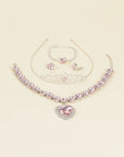 A pink and silver jewelry set on a light cream background, featuring a rhinestone-embellished collar necklace with a heart-shaped pendant, a tiara, a bracelet, and matching stud earrings.