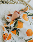 Baby wrapped in a blanket with orange and green pattern, lying on a textured surface.