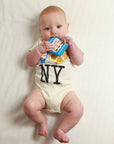 Baby wearing a onesie with 'NY' holding a toy on a white background