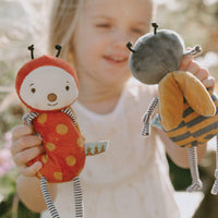 Child holding two plush toys resembling a ladybug and a bee outdoors.