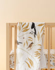 Crib with a white blanket featuring bird and leaf patterns on a beige background