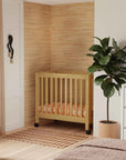 Nursery room with wooden crib, plant, and armchair.