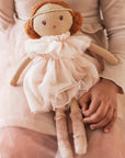 Hand holding a small doll with a delicate dress and red hair.