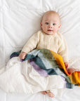 Baby lying on a white blanket with a colorful striped blanket