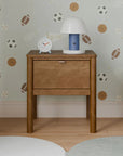 Wooden nightstand with lamp and clock against a wall with sports-themed wallpaper