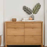 Wooden dresser with decorative items in a room with a white wall and lamp.