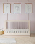 Wooden crib in a room with light pink walls, framed artwork, and decorative items.