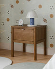 Wooden nightstand with lamp and clock against a wall with sports-themed wallpaper