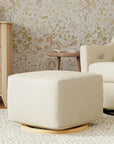 Beige ottoman in a living room with floral wallpaper and a beige armchair.