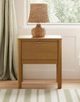 Wooden nightstand with a lamp next to a bed in a bedroom.