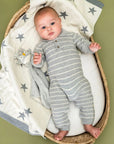 Baby in a striped onesie lying on a star-patterned blanket in a wicker basket.