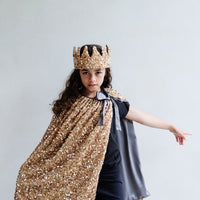 Person wearing a gold sequin cape and crown against a plain background