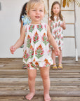 Two young girls in floral dresses standing on a wooden deck.