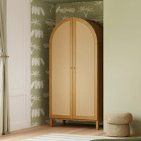 Wooden wardrobe with wicker doors in a room with patterned wallpaper and a small ottoman.