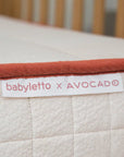 Close-up of a baby crib mattress with 'babyletto x AVOCADO' label.