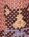 A close-up of a beaded textile or wall art piece featuring a stylized face made of translucent glass beads. The design includes a dusty rose background, dark brown and amber facial features, and light blue beads along the bottom edge.