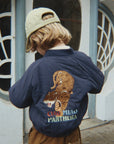 Person wearing a navy blue jacket with a tiger design and 'CIAO MIAO PANTEONA' text, standing in front of a decorative door.
