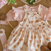 Children's dress with heart and flower pattern, surrounded by accessories on a wooden surface.