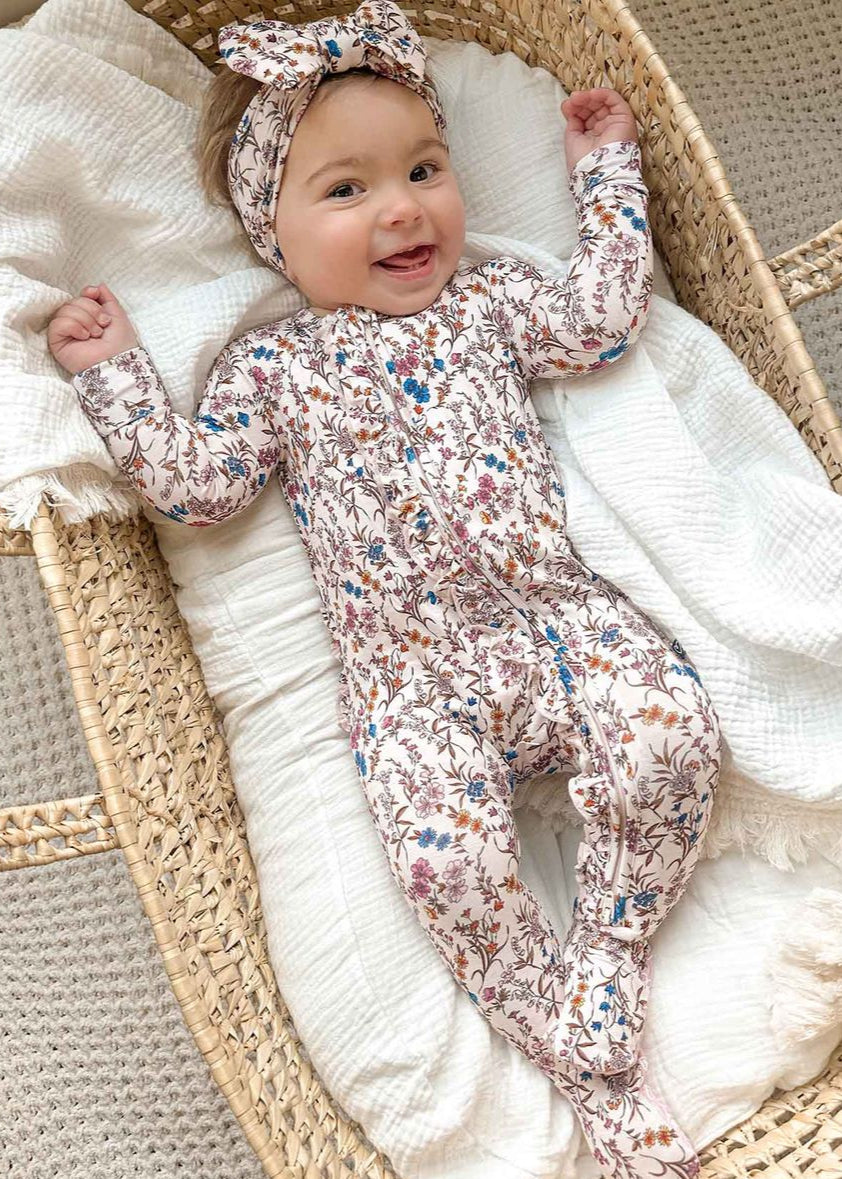 Baby in a floral onesie and headband lying in a woven basket with white blanket