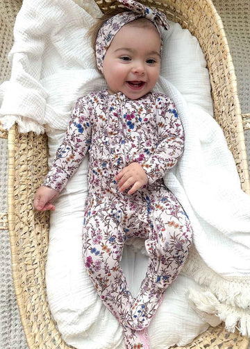 Baby in a floral onesie lying in a moses basket with white bedding