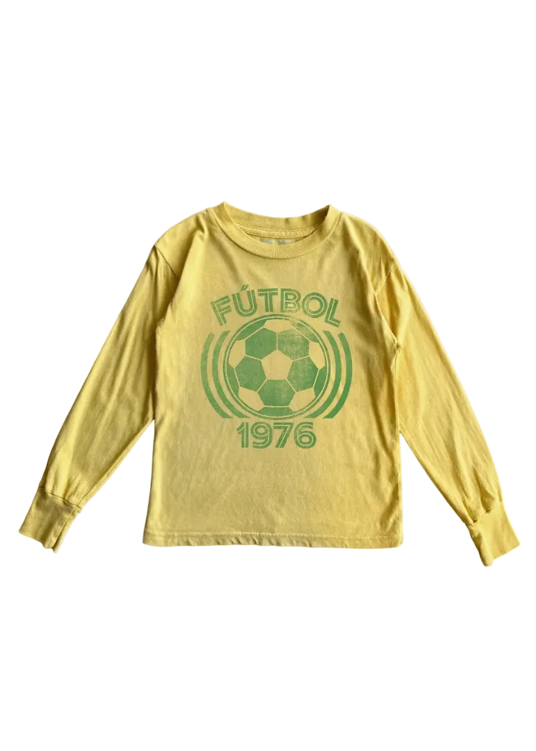 A yellow long-sleeve t-shirt with a green distressed graphic on the front featuring a soccer ball, the word 'FÚTBOl', and the year '1976'.