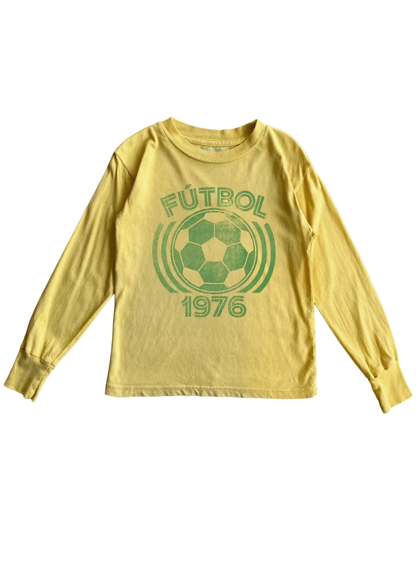 A yellow long-sleeve t-shirt with a green distressed graphic on the front featuring a soccer ball, the word 'FÚTBOl', and the year '1976'.