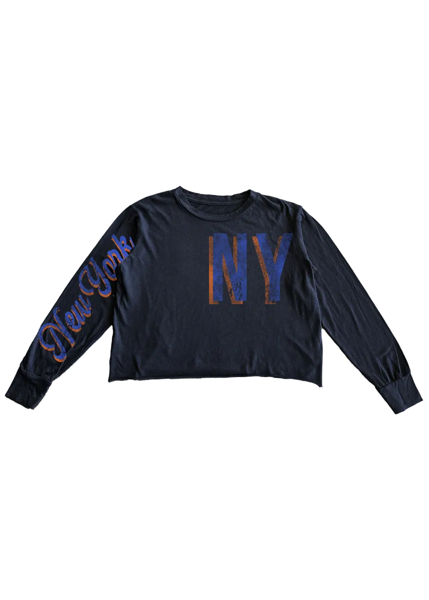 A dark navy blue long-sleeve crop top featuring a distressed blue and orange 'NY' graphic on the chest and 'New York' script on the right sleeve, laid flat against a white background.